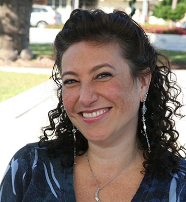 a woman with curly hair and long earrings smiles